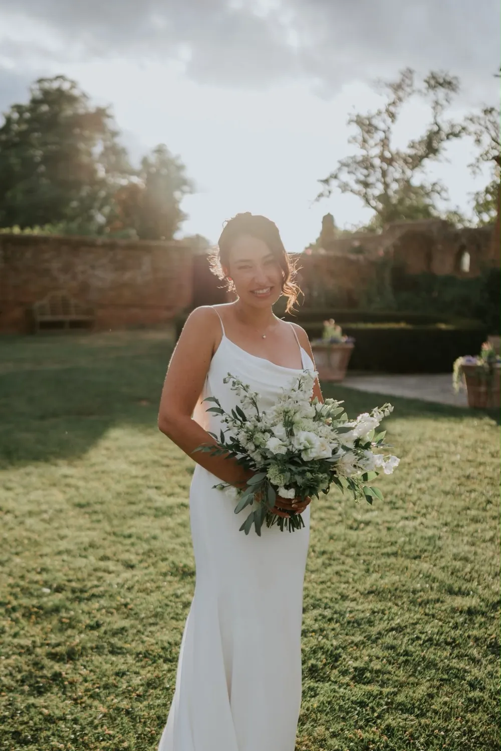 Bride smiling in the garden with her bouquet in golden evening light