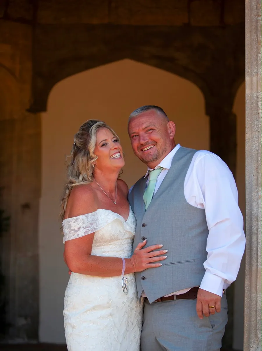 Bride and groom smiling together beneath a stone archway