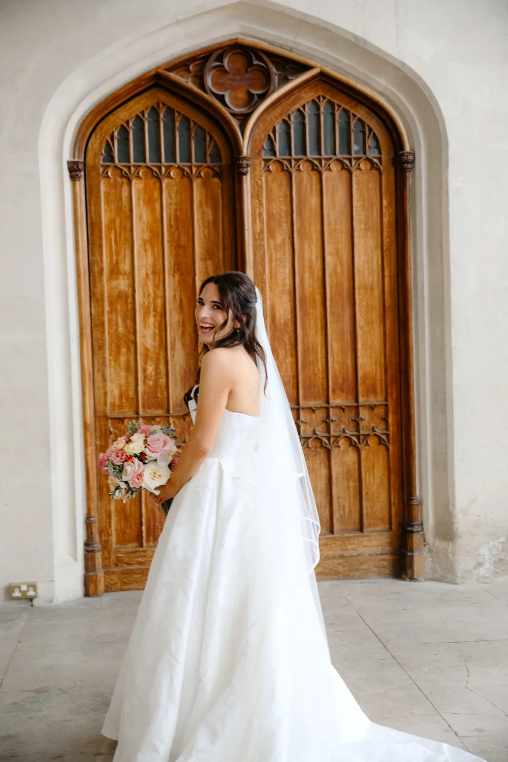 Bride in her veil laughing in front of a pair of old wooden doors